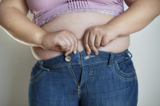 Overweight woman trying to fasten very tight jeans